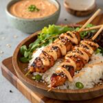 Close-up of juicy grilled Bang Bang chicken skewers served over fluffy white rice, drizzled with creamy spicy sauce and sprinkled with sesame seeds, garnished with fresh greens